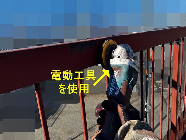 甲府市で屋上の鉄部手すり・鉄部柵に、電動工具（サンダー）でケレン作業（研磨・目粗し）する様子
