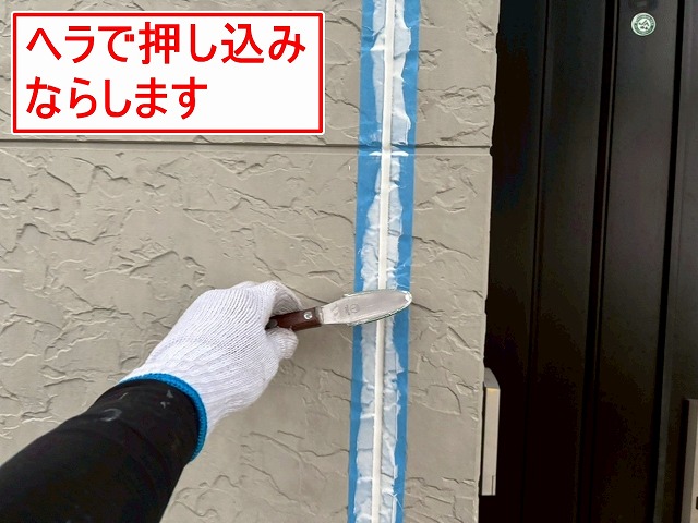 笛吹市でサイディング外壁目地の打ち替え工事を行う様子（ヘラで押し込み均します）